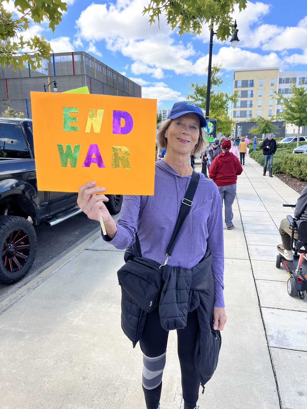 A smiling woman in a blue cap holding an orange sign that reads End War.