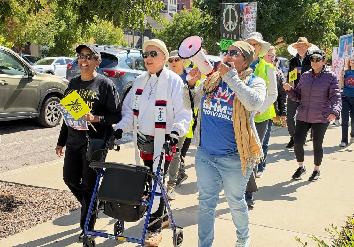 Marchers walking down the sidewalk toward Railroad Park, one holding a megaphone.