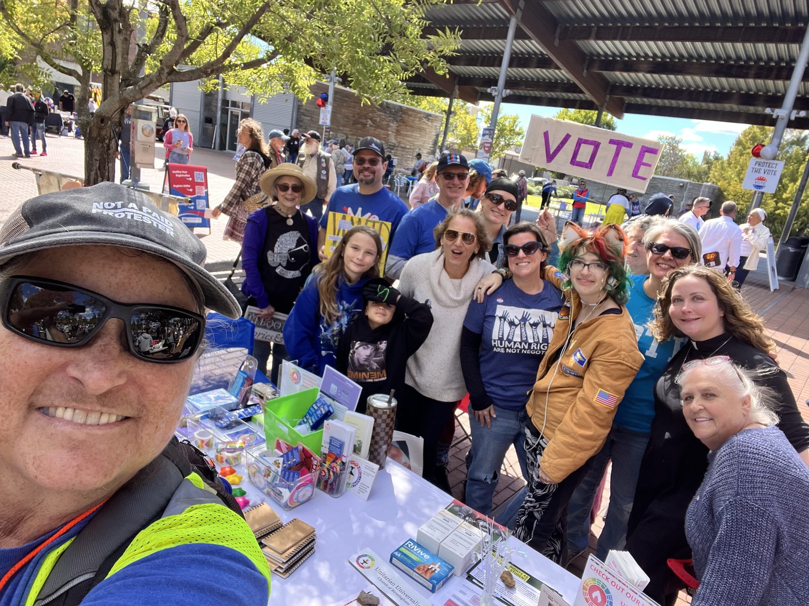 A group of smiling volunteers and partners gathered behind a tabling area at Railroad Park.