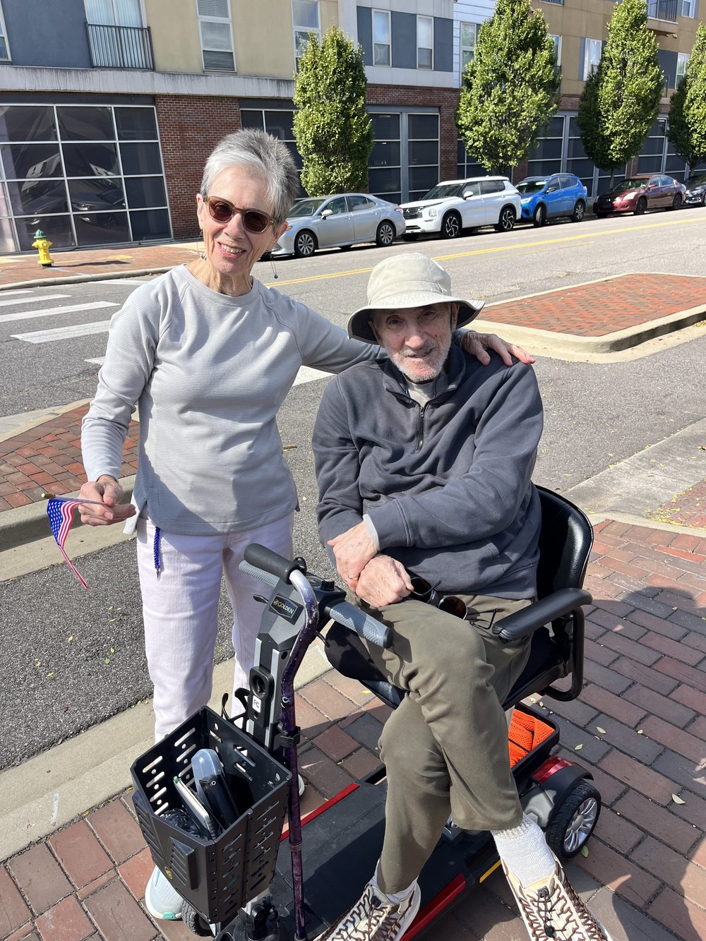 Two smiling rally-goers on a city sidewalk, one holding a small American flag.